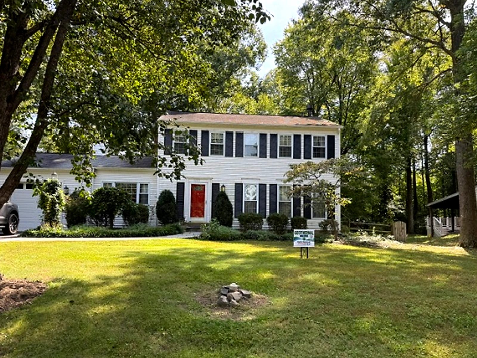 A white colonial house under mature trees with a North American GeoThermal sign in the yard